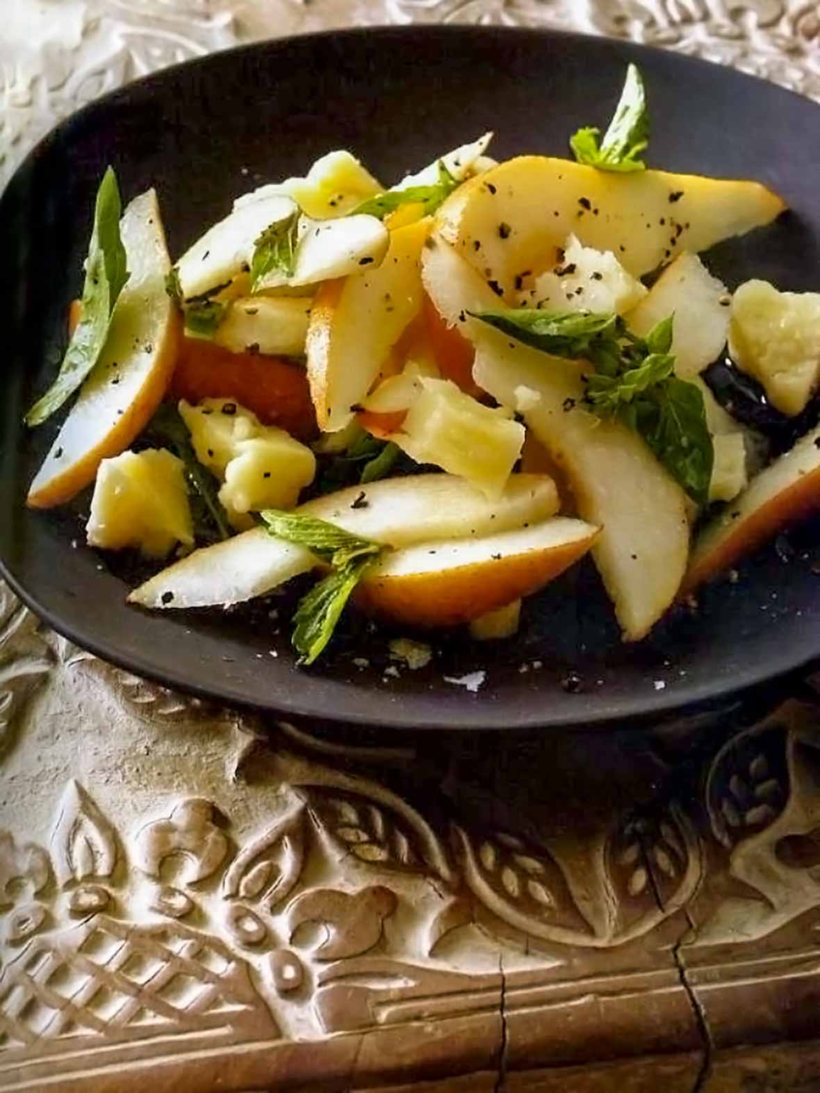 Pear basil pecorino Toscano salad in a large brown serving bowl on a carved wooden tray