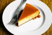 A slice of pure pumpkin cheesecake on a white plate drizzled with caramel glaze with a fork resting beside it.