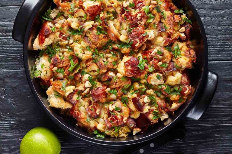 A black bowl of bread stuffing with herbs and bacon, alongside is a green apple.