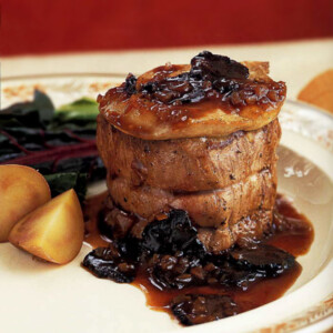 Medallions of beef with foie gras and truffles on a white plate, drizzled with gravy and flanked with roasted potatoes.