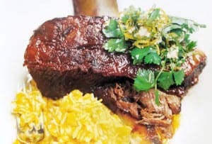 Braised short ribs on a plate with pumpkin orzo, garnished with parsley