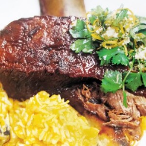 Braised short ribs on a plate with pumpkin orzo, garnished with parsley