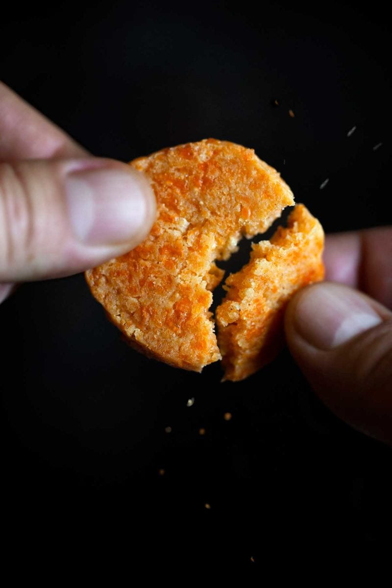 A person breaking a Cheddar-Parmesan cracker in half.
