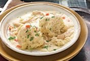 A bowl of chicken ad dumplings on a plate resting on an antique tray.