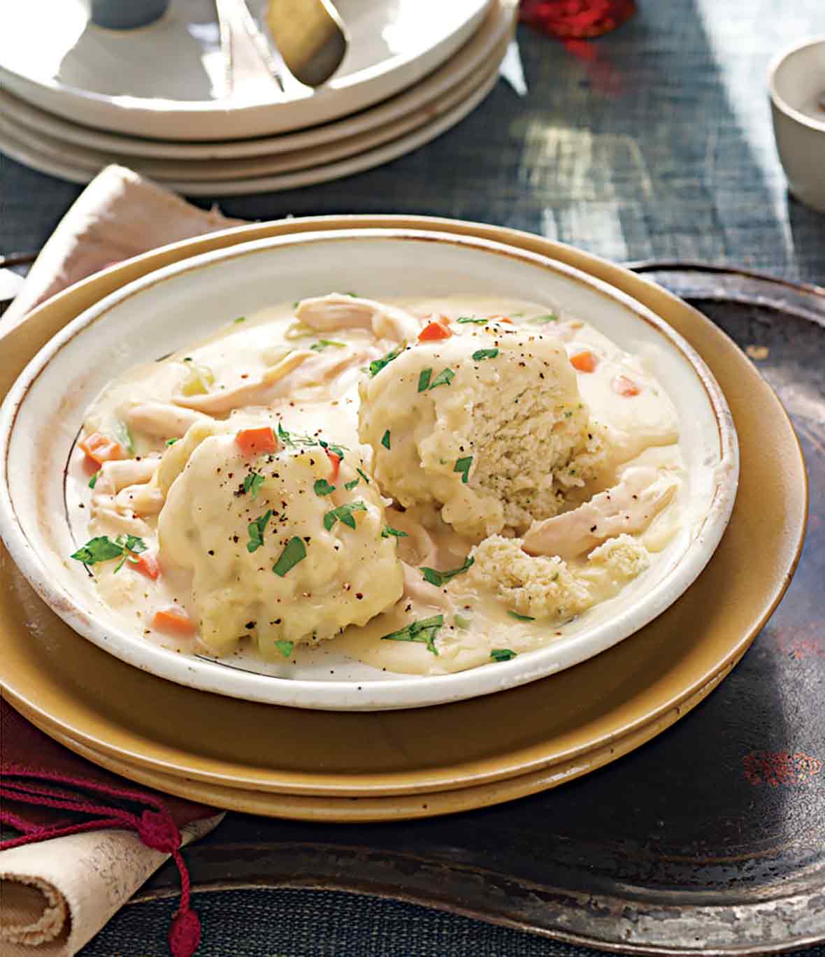 A bowl of chicken ad dumplings on a plate resting on an antique tray.
