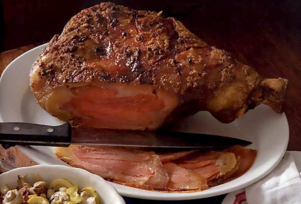 A baked country ham on an oval platter with a knife resting beside it.