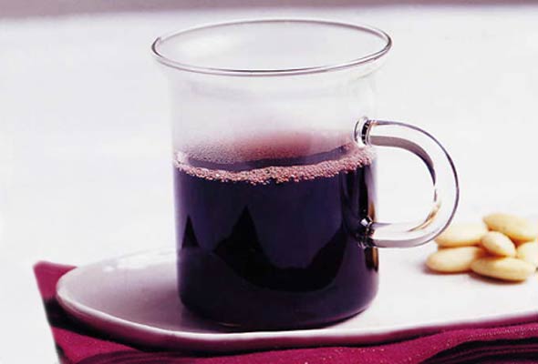 A glass mug of glogg aquavit on a white saucer with a pile of almonds on a red placemat.