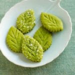 White plate with five green leaf-shaped cookies with coarse sugar on top