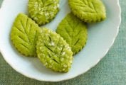 White plate with five green leaf-shaped cookies with coarse sugar on top