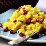 Persian rice pilaf piled on a square blue plate, garnished with pomegranate seeds and sliced green onions.