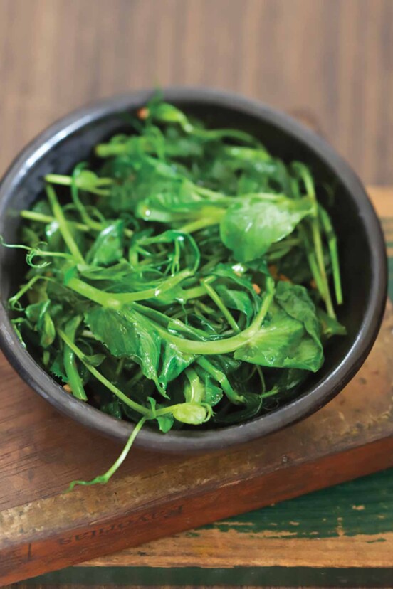 A brown bowl filled with stir-fried pea shoots.