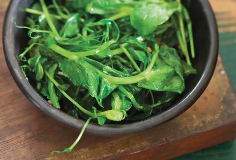 A brown bowl filled with stir-fried pea shoots