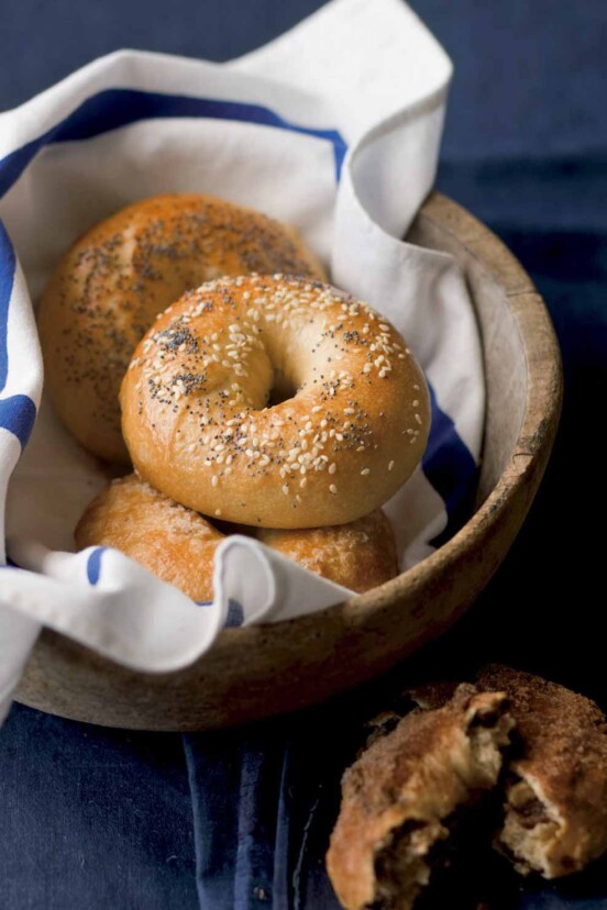 Basket of homemade bagels topped with sesame seeds and poppy seeds, raisin bagel on the side