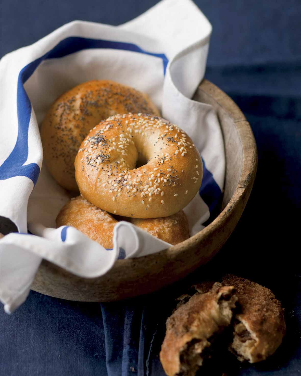 Basket of homemade bagels topped with sesame seeds and poppy seeds, raisin bagel on the side