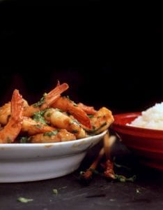 A white bowl piled with spicy shrimp and a red bowl of white rice