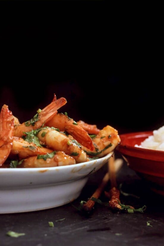 A white bowl piled with spicy shrimp and a red bowl of white rice
