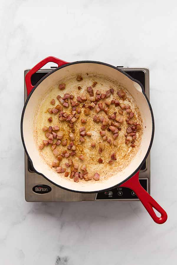 Crisping pancetta cubes in a skillet for spaghetti carbonara.