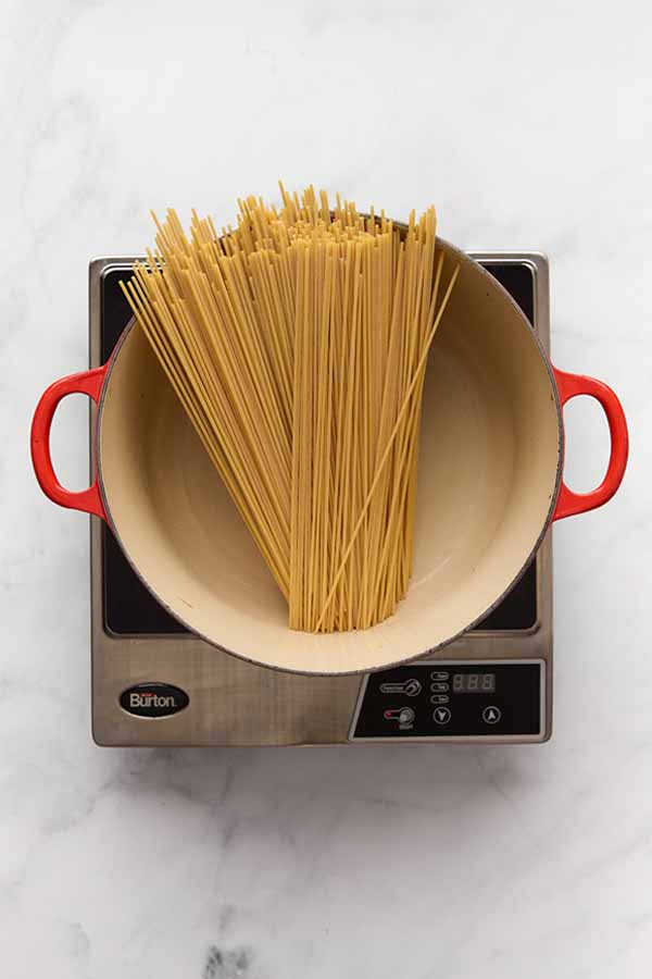 Uncooked spaghetti resting in a pot of boiling water for carbonara.