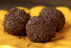 Three golf-ball size chocolate Brazilian candies covered with chocolate sprinkles on a yellow plate.