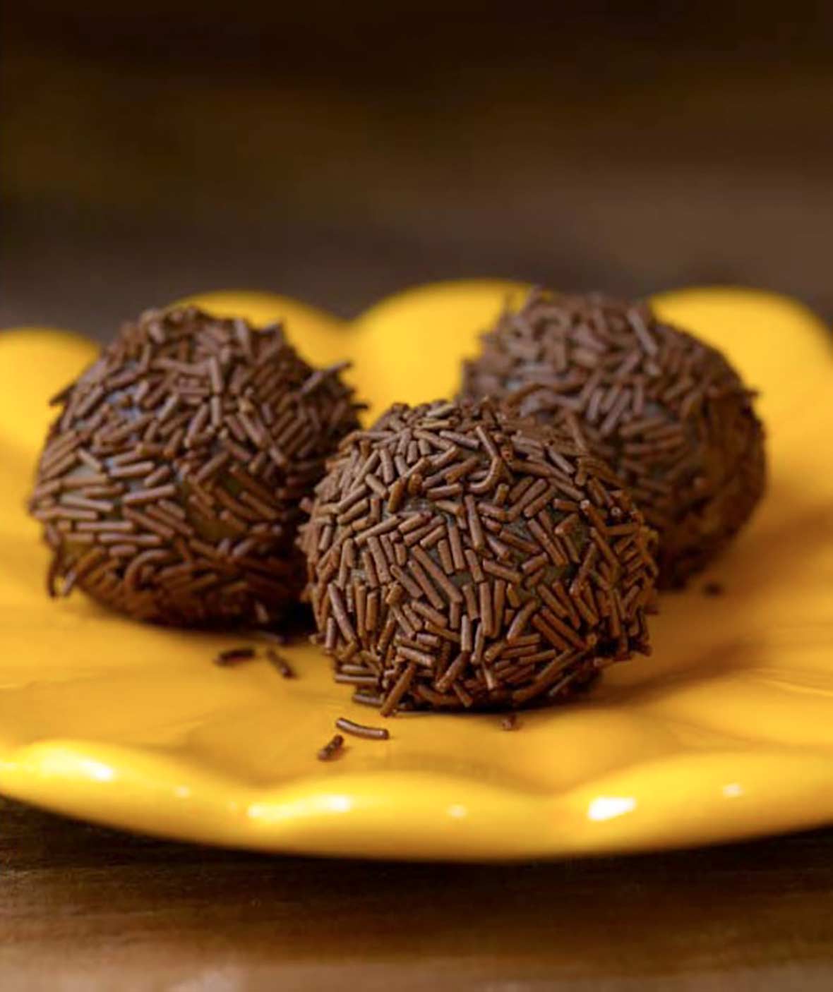 Three golf-ball size chocolate Brazilian candies covered with chocolate sprinkles on a yellow plate.