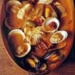 Copper pot with seafood soup with fish fillets, clams, mussels, olives, tomato broth