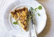A slice of butternut squash and Parmesan tart on a white plate with a fork and knife, garnished with microgreens.