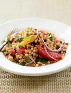 A white bowl filled with fregola salad with fresh citrus and red onion and mint leaves on a woven placemat.