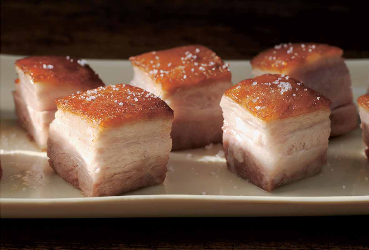 Cubes of pork belly confit on a white serving platter.