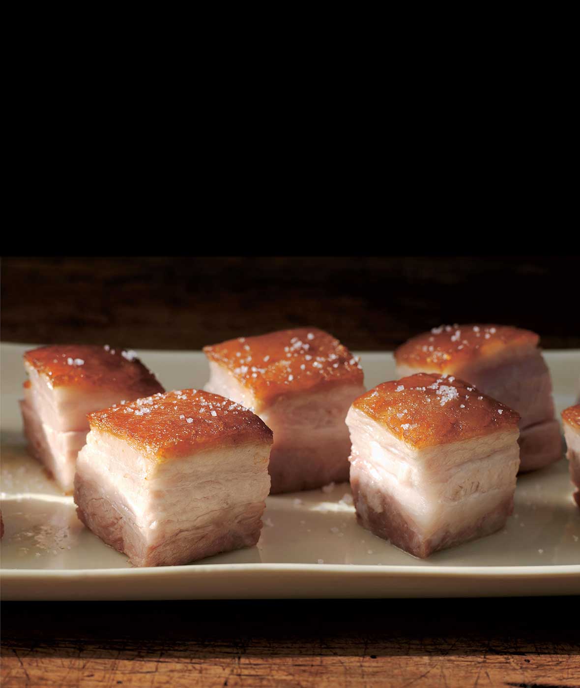 Cubes of pork belly confit on a white serving platter.