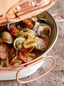 A cataplana with slices of spicy chouriço sausage and sweet clams in a tomato-onion broth.