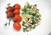 A white plate with a mound of cannellini bean salad and a bunch of grape tomatoes on the vine.