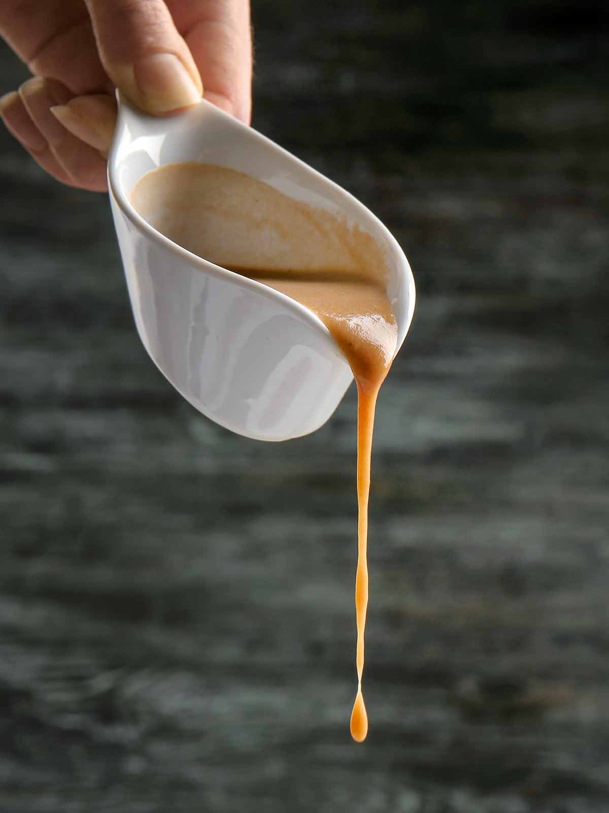 Chicken gravy being poured out of a white gravy boat.