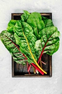Leaves of colorful rainbow Swiss chard sitting in a wooden box.