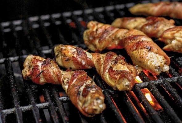 Bacon-wrapped chicken wings, secured with toothpicks on an open grill.