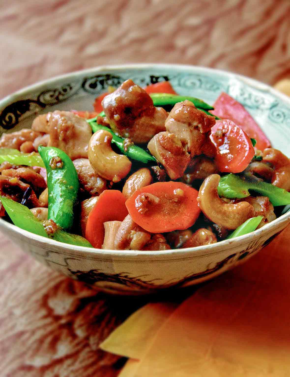 Bowl of cashew chicken with chunks of stir-fried chicken, carrots, sugar snap peas, celery, cashews.