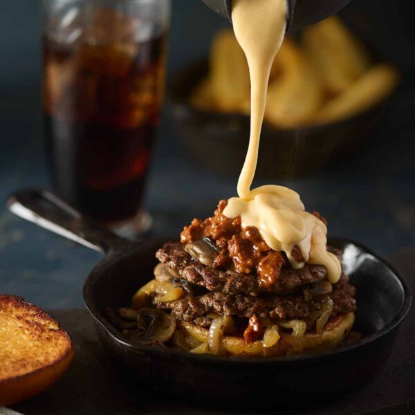 A silky cheddar cheese pouring over an open-faced burger.