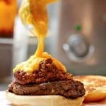 A chili cheddar burger on a bun half with cheese sauce being poured over it.