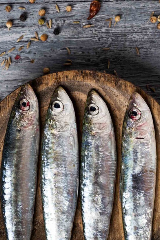 A close up shot of 4 whole sardines on a wooden plate.