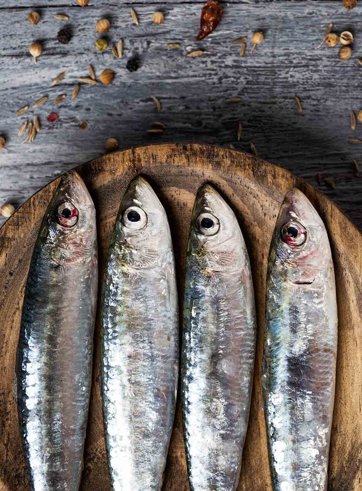 A close up shot of 4 whole sardines on a wooden plate.