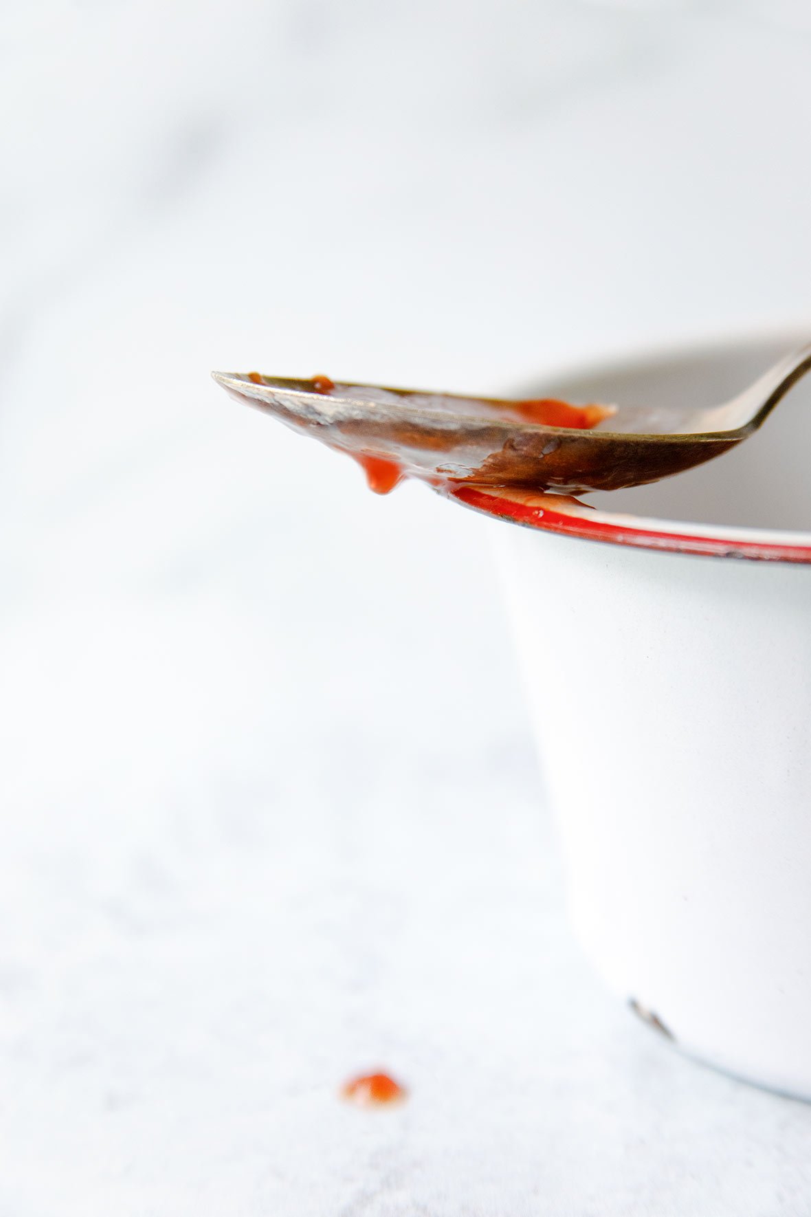 A spoon dripping with strawberry jam, resting on the edge of an enamel pot.