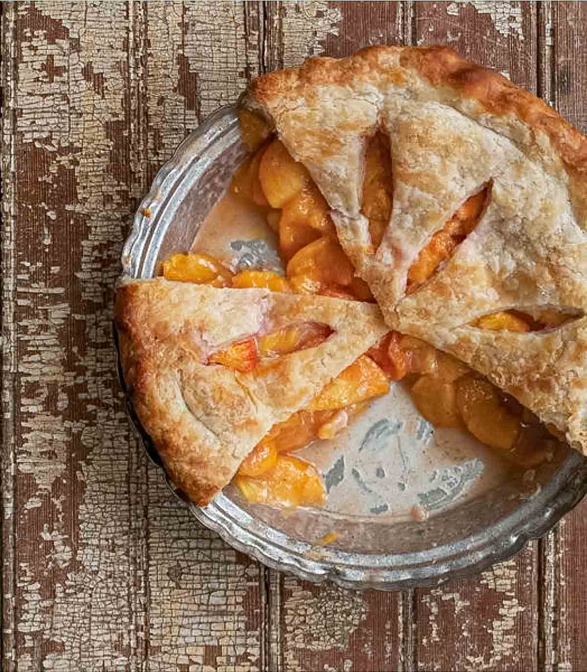 A baked fresh peach pie with three slices missing.