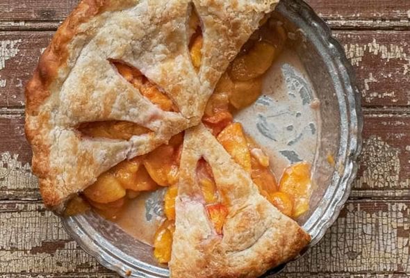 A baked fresh peach pie with three slices missing.