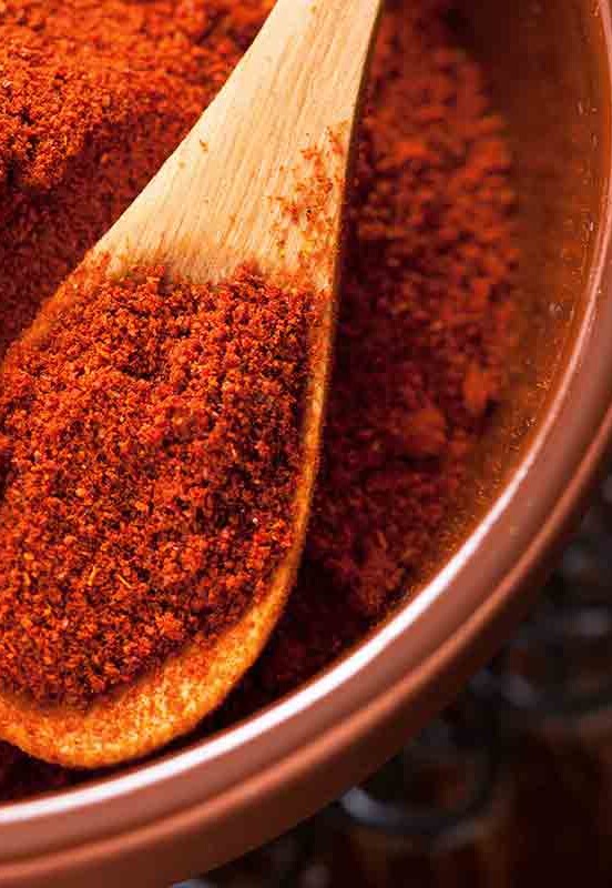 A bowl filled with paprika with a small wooden spoon resting inside.