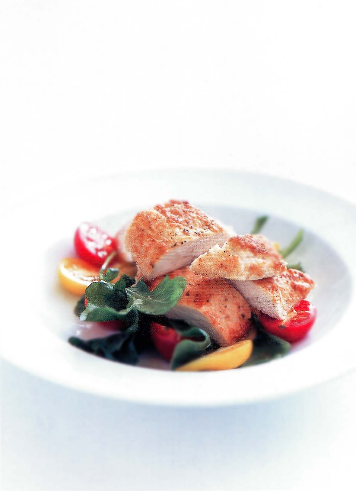 White bowl of sliced parmesan-crusted chicken, lettuce, and red and yellow cherry tomatoes