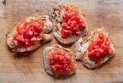 Four slices of bruschetta topped with tomato on a wooden cutting board.