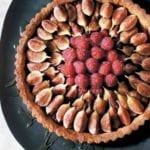 A fresh fig and raspberry tart drizzled with honey on a black platter.
