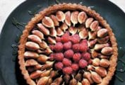 A fresh fig and raspberry tart drizzled with honey on a black platter.