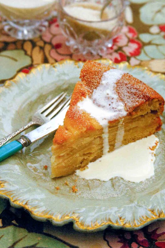 A decorative plate topped with a slice of drunken apple cake that is drizzled with cream.
