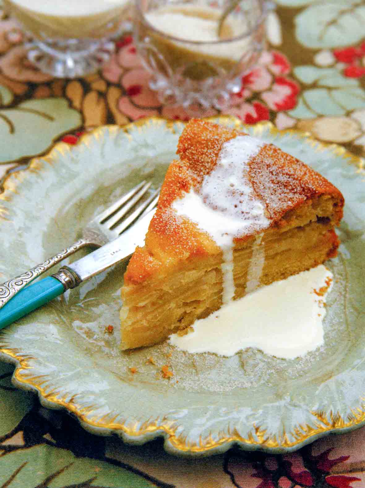 A decorative plate topped with a slice of drunken apple cake that is drizzled with cream.