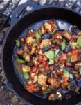 Skillet on a grill filled with eggplant caponata--chopped eggplant, onions, fennel, onions, almonds, basil